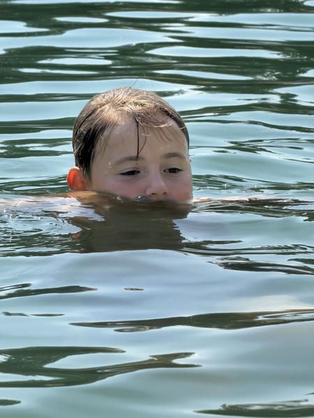 A young child's head emerges from the calm, rippling water, their expression focused and serene